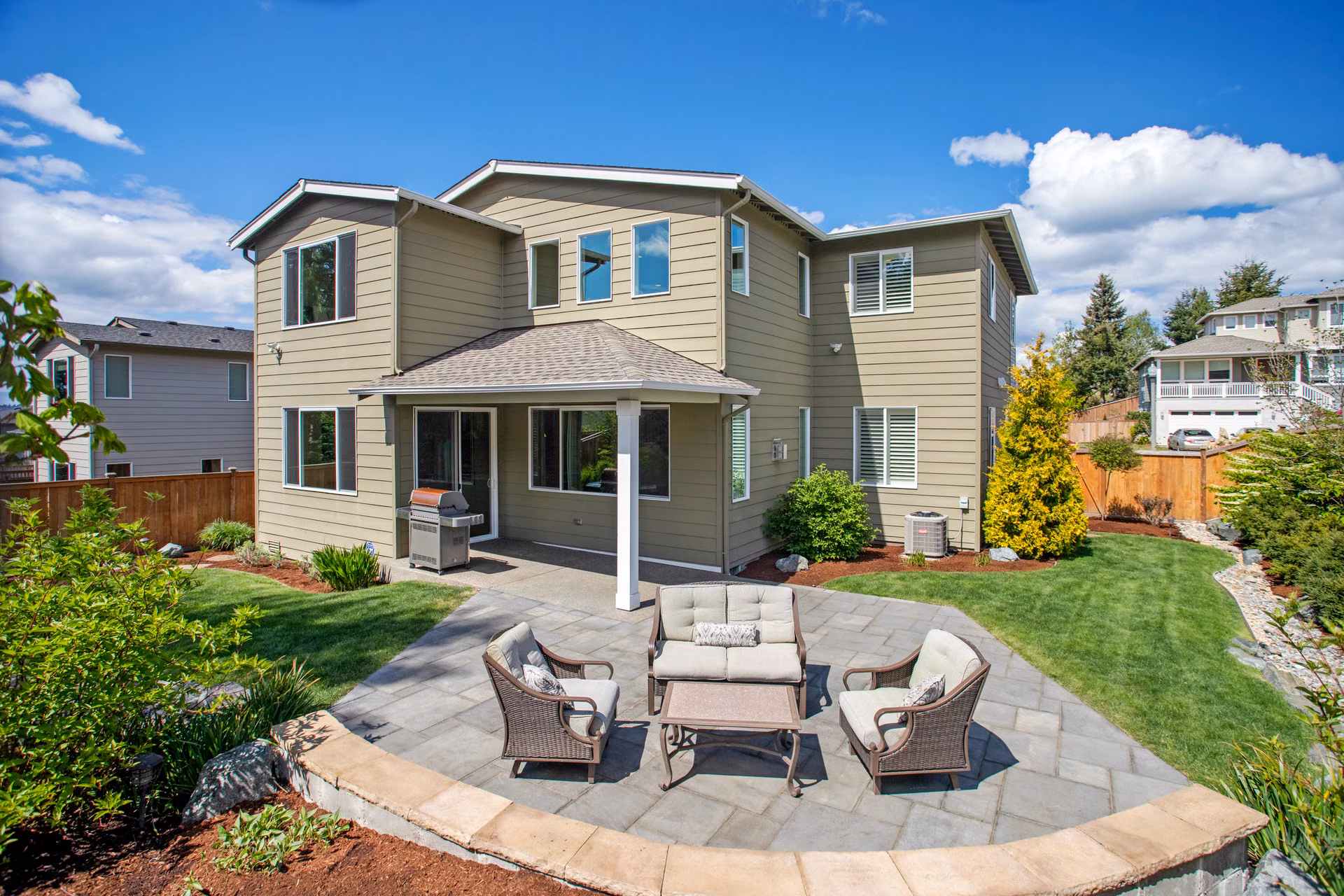 Curved paver patio with outdoor seating behind a two-story home